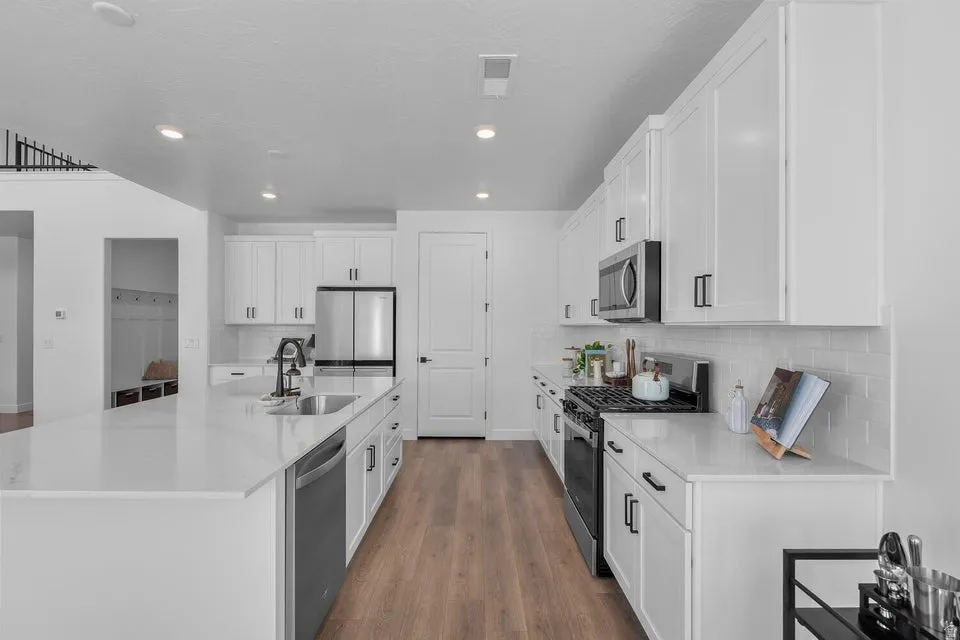 Well-appointed kitchen featuring white cabinetry, stainless steel appliances, a large center island with an undermount sink, and wood-finish flooring