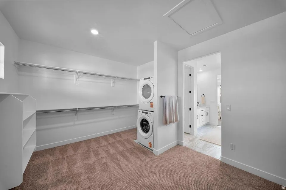 Expansive closet space featuring dual hanging rods, built-in shelving, stacked laundry appliances, and recessed lighting