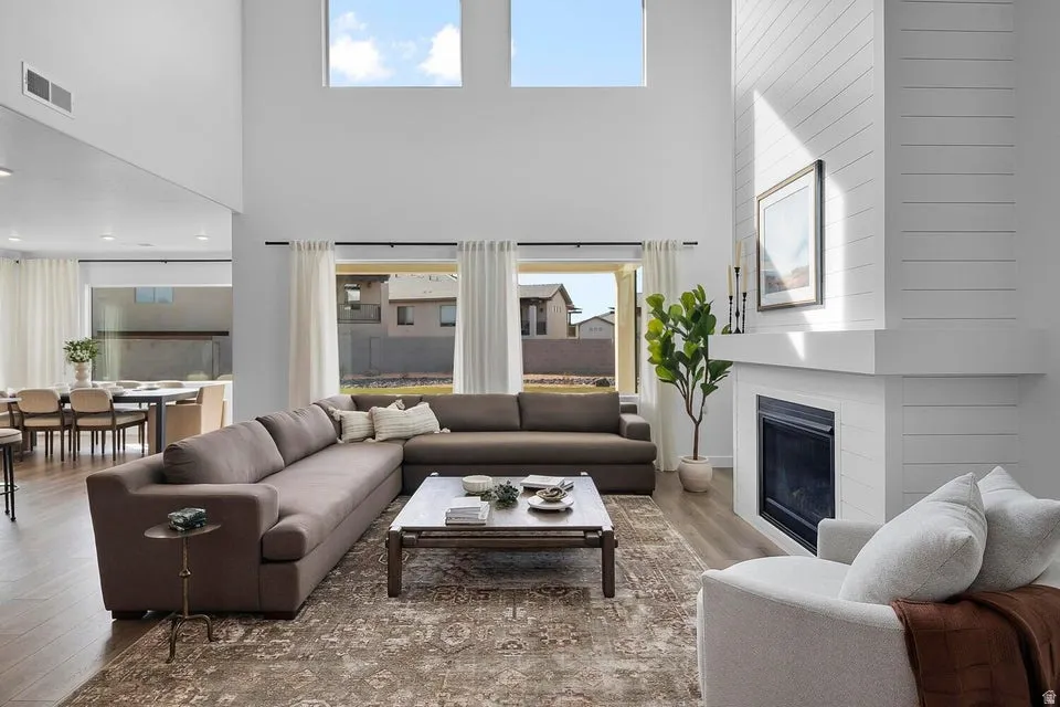 Two-story living area with wood-finish flooring, a contemporary fireplace with shiplap accent, and large windows