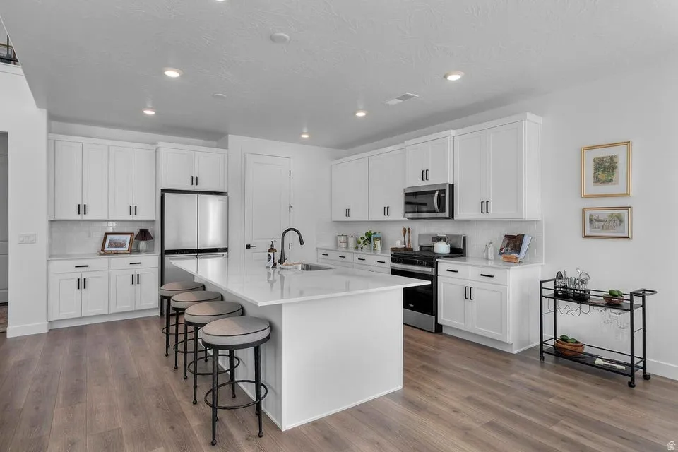 Modern kitchen featuring white cabinetry, a large center island with seating, stainless steel appliances, a tile backsplash, and wood-finish flooring