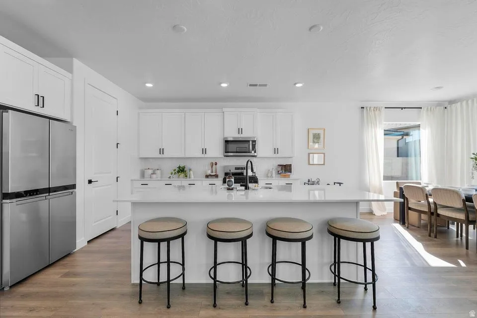 Open-concept kitchen featuring white shaker cabinetry, stainless steel appliances, a center island with countertop seating, and wood-finish flooring