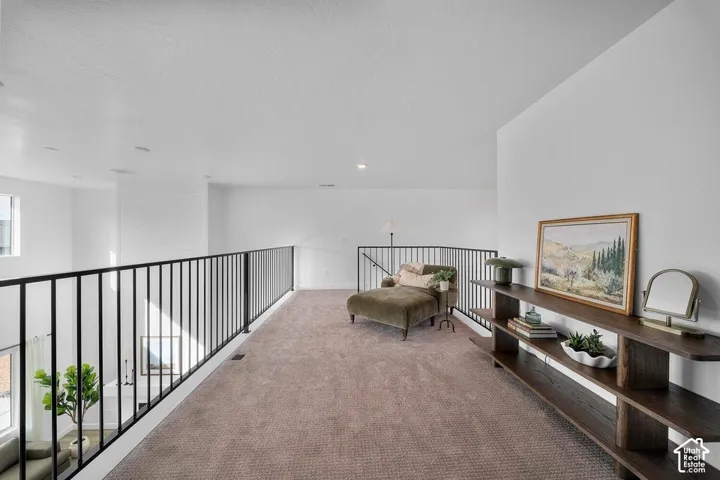 Spacious loft area featuring carpeting, white walls, black metal railing, and a built-in dark wood shelving unit