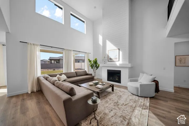 Two-story living area with high ceilings, multiple large windows, wood-finish flooring, a white brick-finish fireplace, and an upper-level balcony