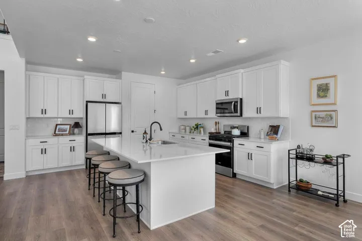 Modern kitchen featuring white cabinetry, a large center island with seating, stainless steel appliances, a tile backsplash, and wood-finish flooring
