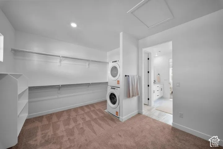 Expansive closet space featuring dual hanging rods, built-in shelving, stacked laundry appliances, and recessed lighting