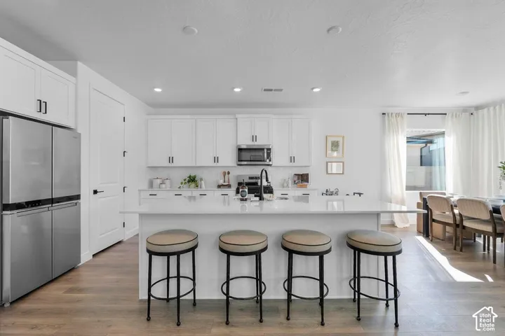 Open-concept kitchen featuring white shaker cabinetry, stainless steel appliances, a center island with countertop seating, and wood-finish flooring