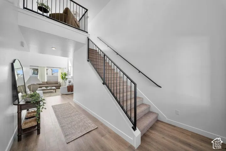 Wood-finish flooring, carpeted staircase with dark metal railing, and an upper-level balcony with a matching dark metal railing