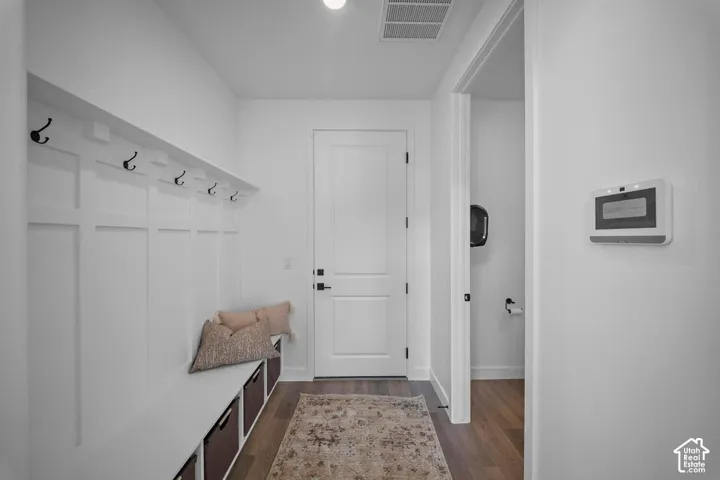 Board and batten wall with integrated bench seating, black coat hooks, wood-finish flooring, and a solid panel interior door with matte black hardware