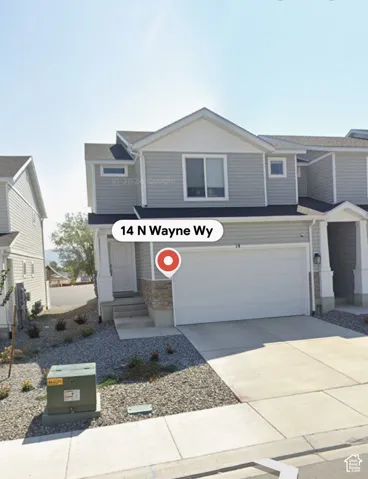 Two-story exterior with light gray siding, white trim, attached garage, stone accents, and paved driveway