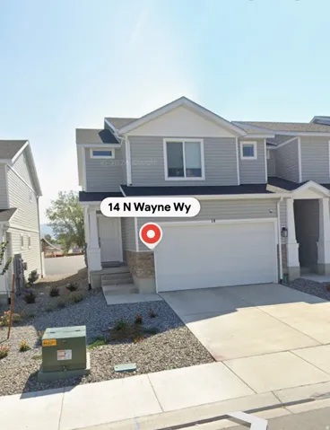 Two-story exterior with light gray siding, white trim, attached garage, stone accents, and paved driveway