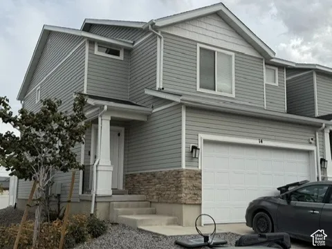 Two-story exterior featuring horizontal siding, decorative stone veneer, gable roofline, covered entry with a column, and a double-car garage