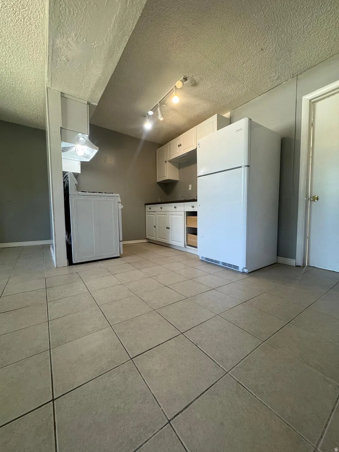 Ceramic tile flooring, white cabinetry, dark countertops, white refrigerator, and track lighting