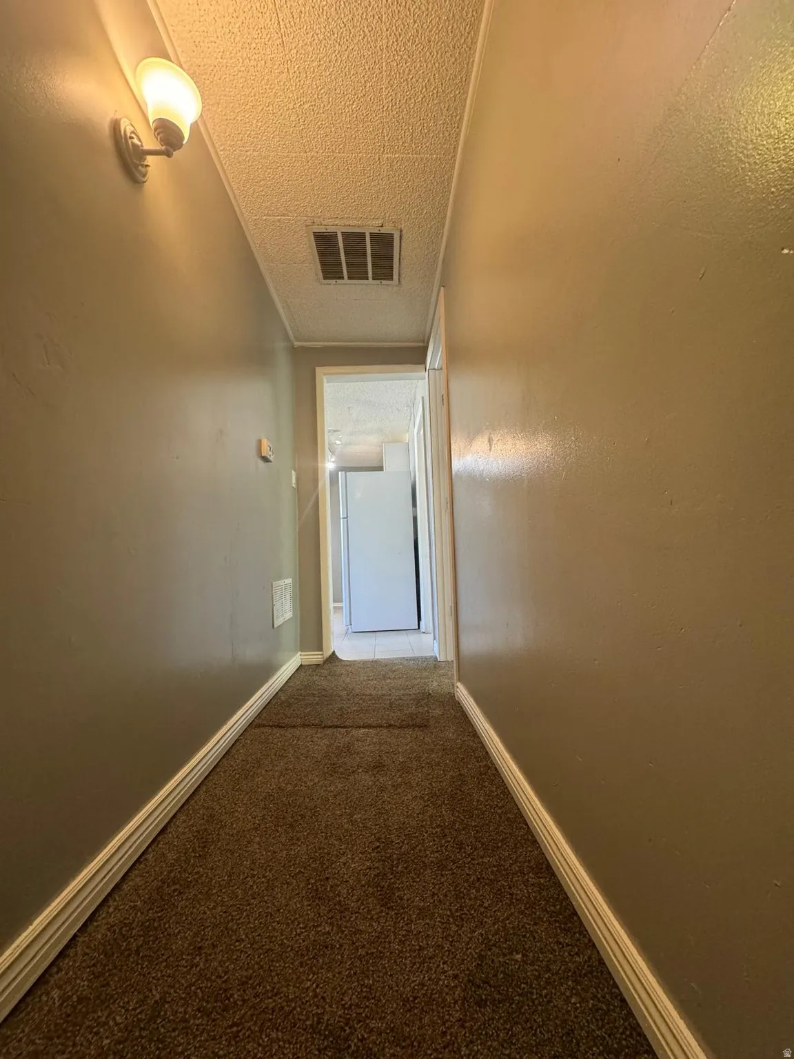 Textured ceiling with recessed vent, wall sconce lighting, and carpet flooring