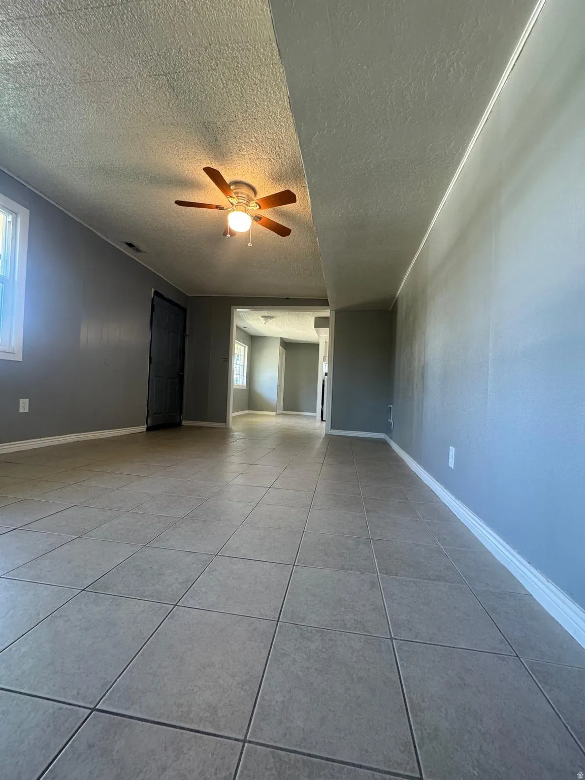 Spacious room featuring tile flooring, painted walls, and a ceiling fan with integrated lighting
