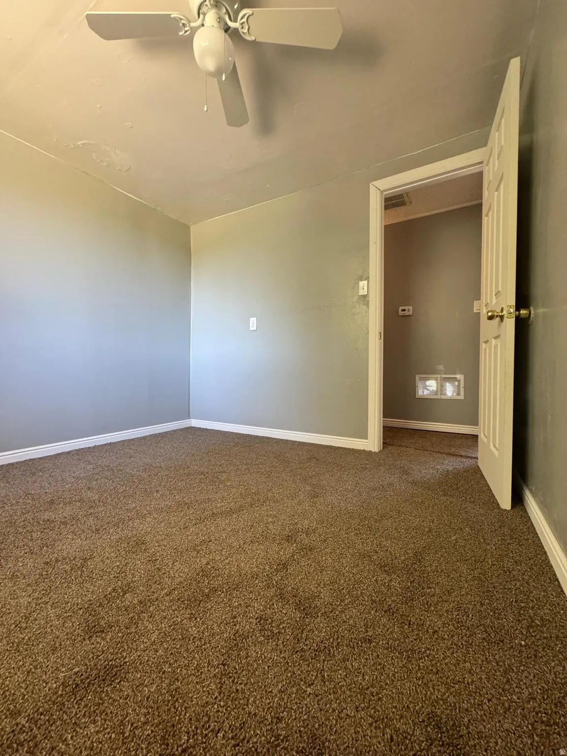 Neutral wall paint, brown carpet flooring, and a white ceiling fan with integrated lighting