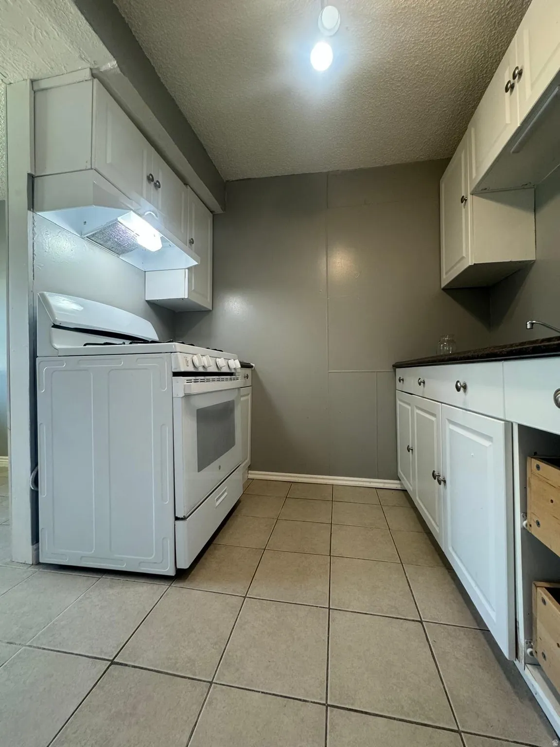 White cabinetry, built-in range hood, white range, tile flooring, and dark countertops