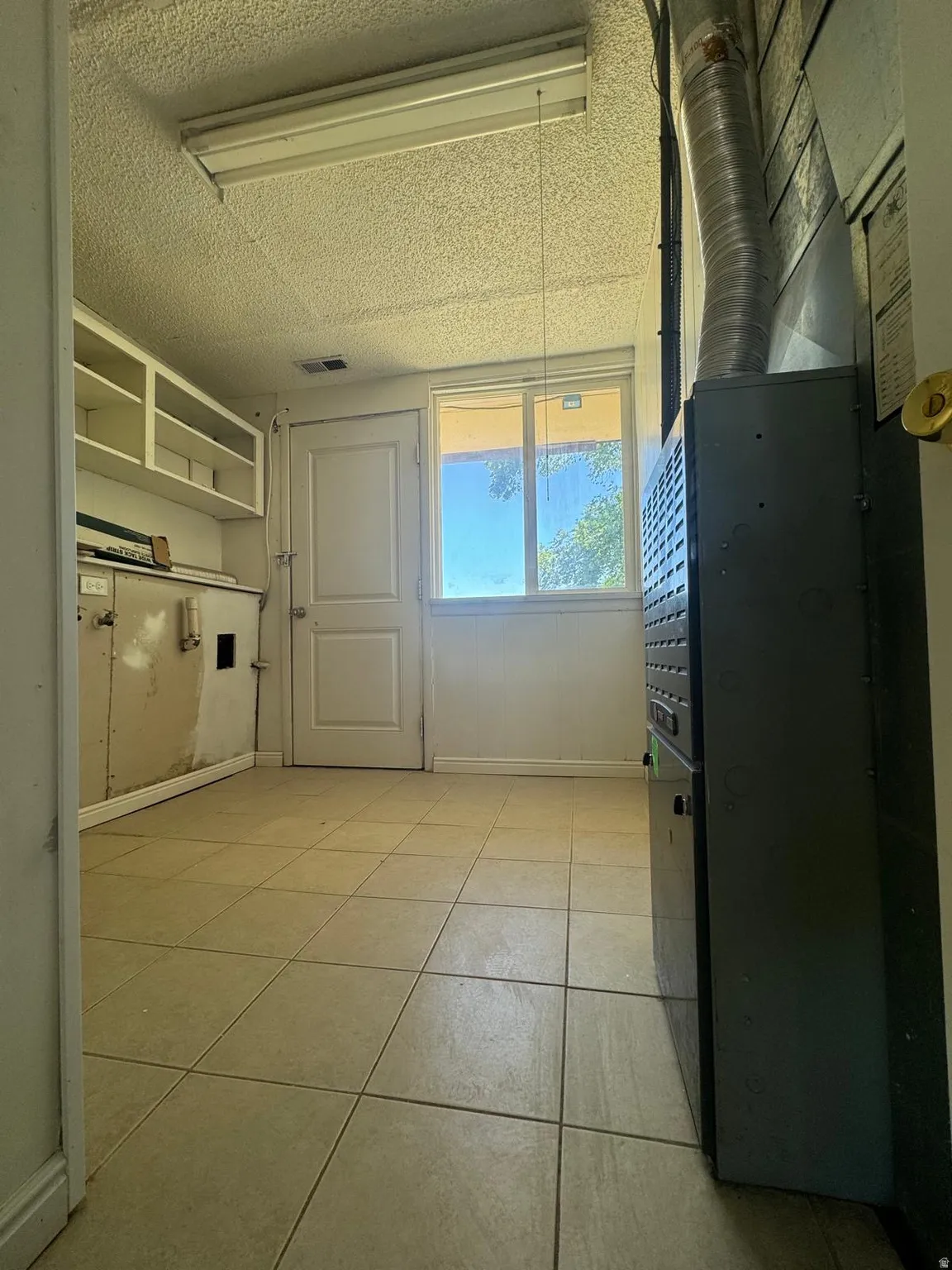 Recessed cabinetry, tile flooring, window, and a utility door