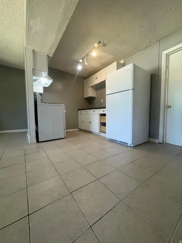 Ceramic tile flooring, white cabinetry, dark countertops, white refrigerator, and track lighting