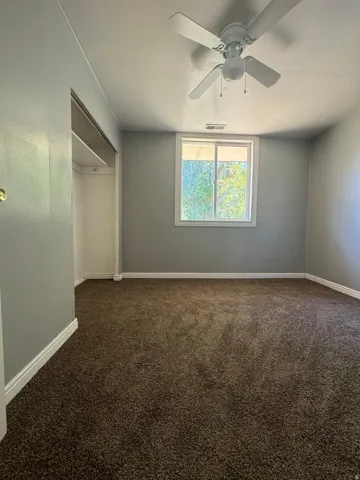 Plush carpet flooring, neutral wall tones, white trim, a multi-pane window, and a ceiling fan with integrated lighting