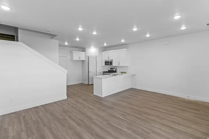 Recessed lighting, wood-finish flooring, white kitchen cabinetry, stainless steel appliances, and a kitchen island with a sink