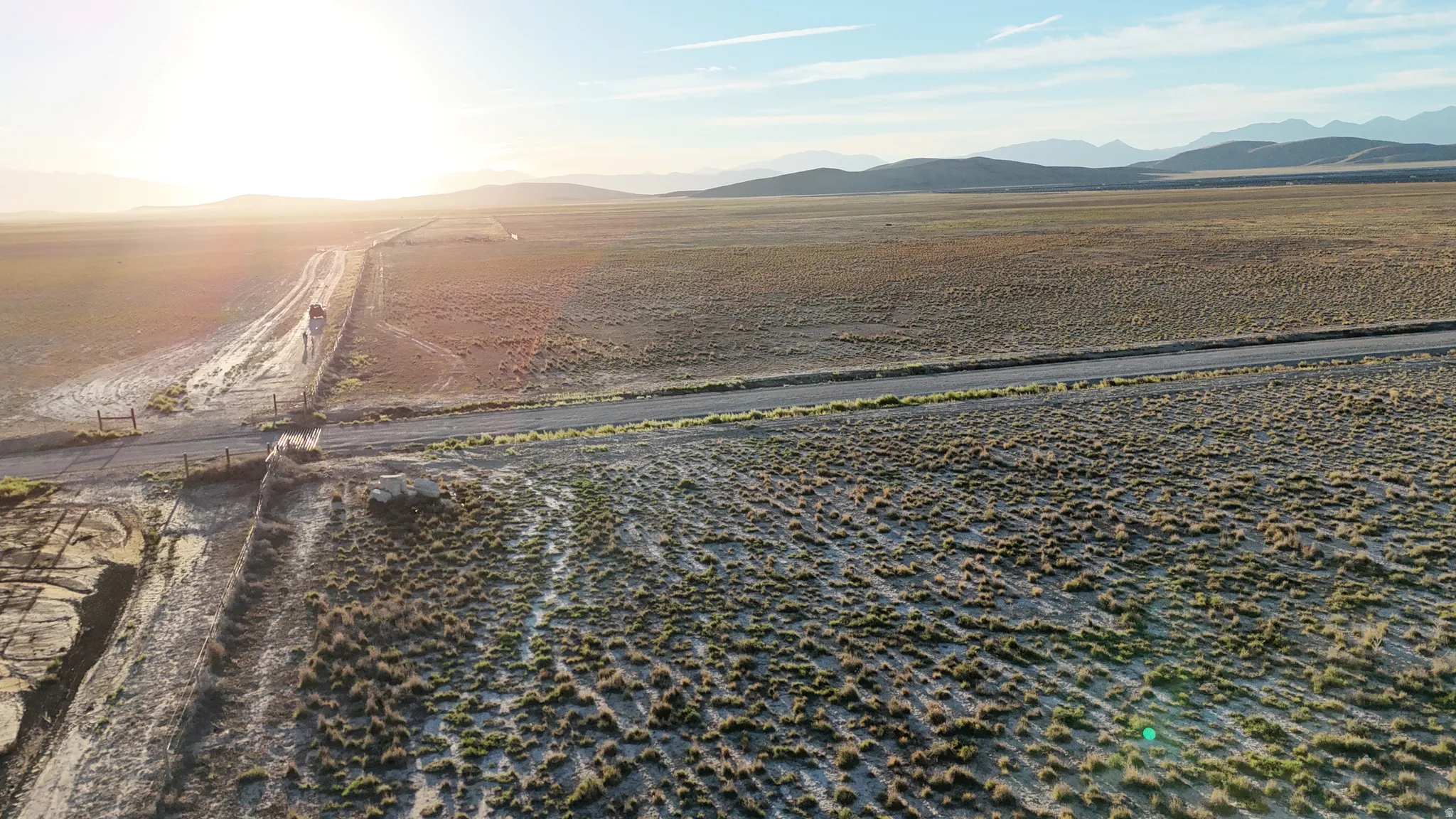 Expansive open terrain with a dirt road, sparse vegetation, and distant mountain ranges