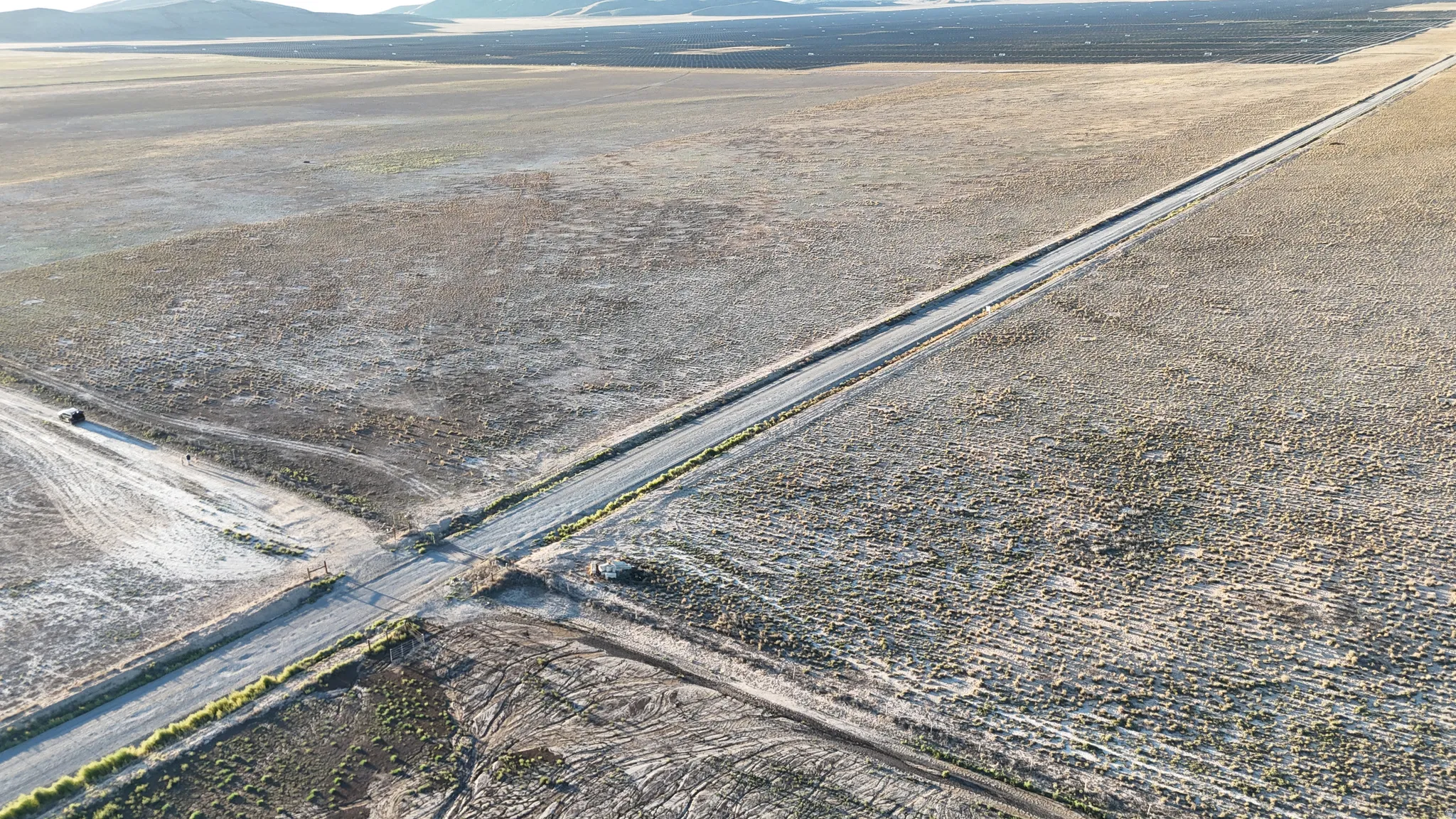 Expansive land parcel featuring a main roadway and intersecting dirt paths, surrounded by a vast, open landscape with distant mountains
