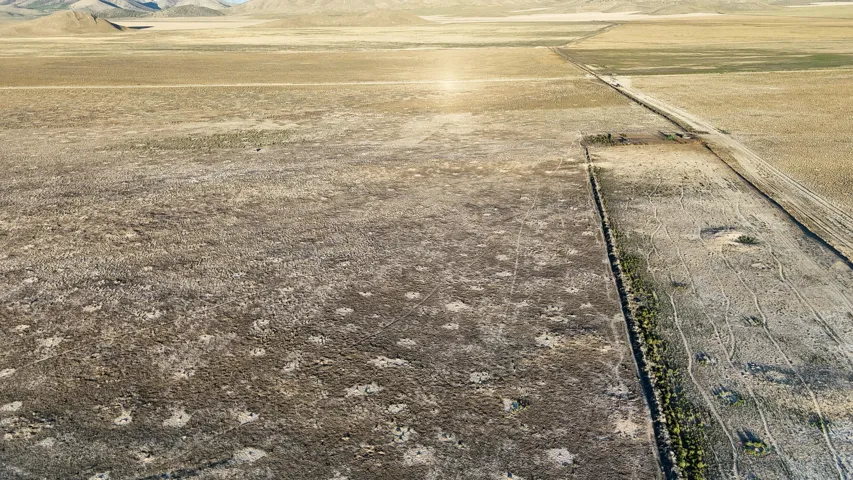 Expansive undeveloped land with natural vegetation, featuring a defined property boundary and distant mountain ranges