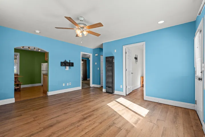 Wood-finish flooring, ceiling fan with integrated lighting, recessed lighting, white trim, and a doorway with an arched opening