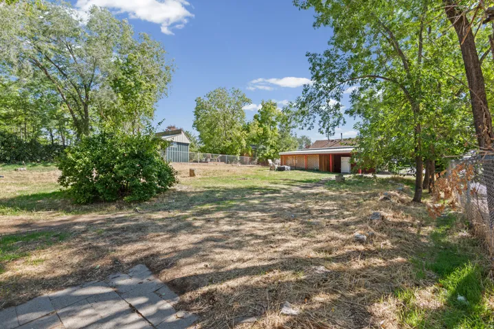 Expansive outdoor area featuring mature trees, a detached storage building, and fencing