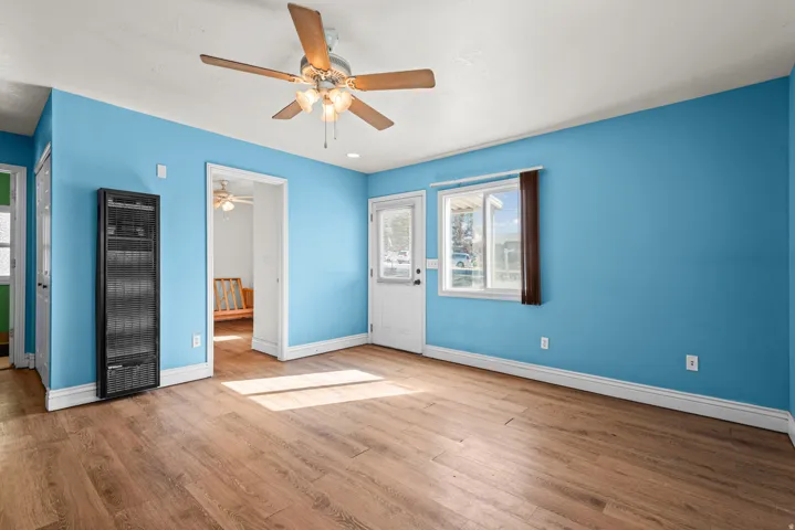 Wood-finish flooring, ceiling fan with integrated lighting, wall-mounted heating unit, and a white paneled door