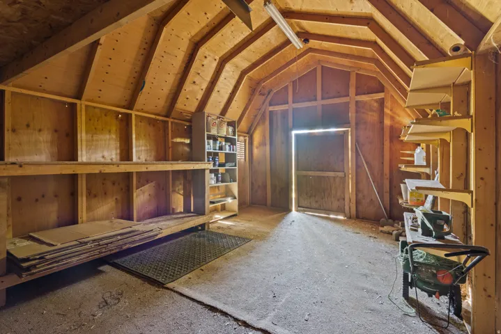 Storage shed with exposed wood framing, built-in shelving, concrete flooring, and a single entry door