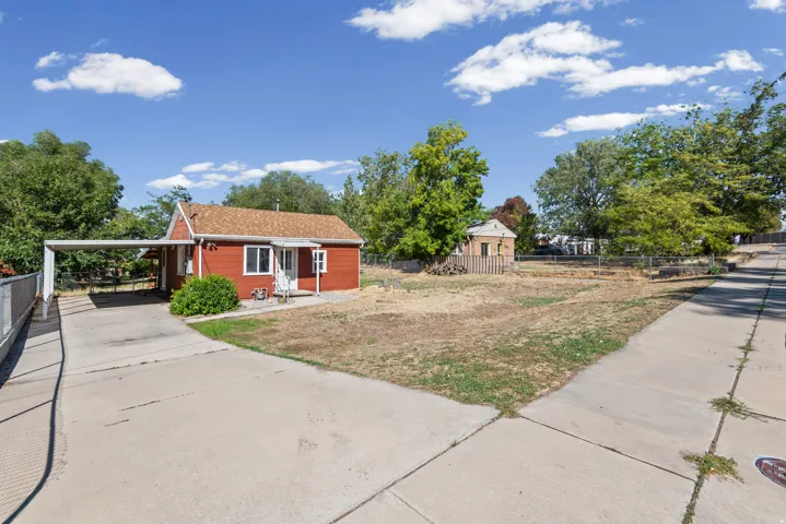 Red exterior siding, carport, concrete driveway, and a detached structure