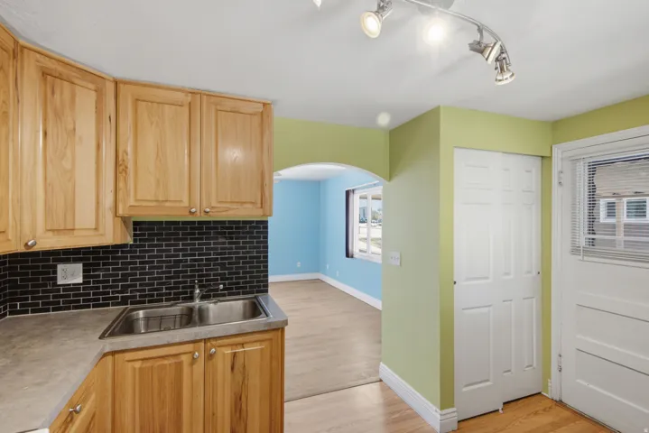 Natural wood cabinetry, stainless steel double basin sink, black subway tile backsplash, and track lighting