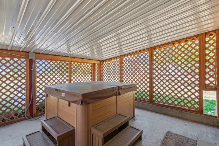 Covered patio featuring a hot tub, wood lattice walls, a corrugated metal ceiling, and a concrete floor