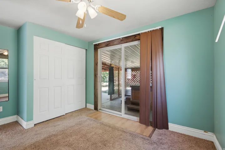 Carpeted flooring with white baseboards, sliding panel closet doors, and a ceiling fan with light fixture