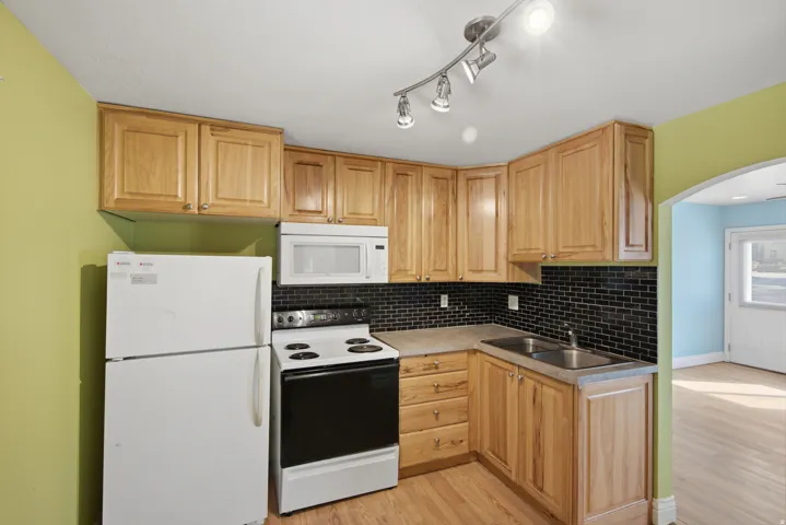 Efficient kitchen featuring natural wood cabinetry, stainless steel appliances, black subway tile backsplash, and wood-finish flooring