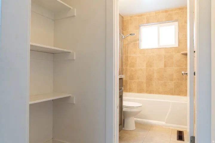 Built-in shelving, full bathroom with tiled walls, showerhead, bathtub, and window