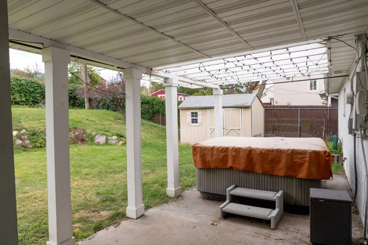 Partially covered patio-hot tub space with white pillars leading to landscaped backyard.