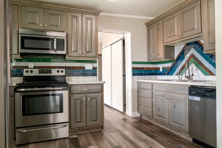 Kitchen featuring stainless steel appliances, cabinetry with wood finish, a distinct tile backsplash, light-toned countertops, and the door to formal dining.