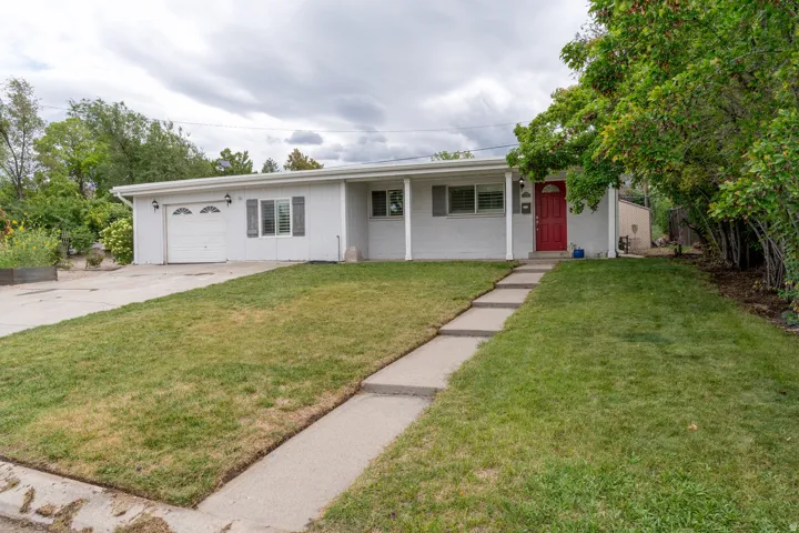 Nice curb appeal for single level residence featuring light-colored siding, a prominent red entry door, an attached garage, nice steps from the street, and a concrete driveway.