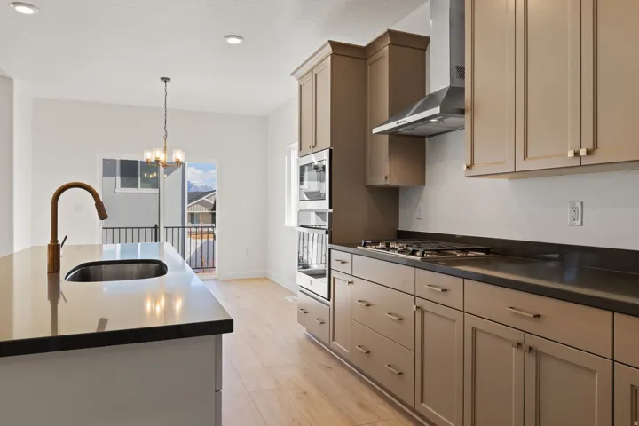 Kitchen featuring an island with an undermount sink and gooseneck faucet, light wood-finish flooring, recessed lighting, and a built-in oven and gas cooktop