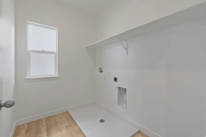 Utility room featuring wood-finish flooring, a double-hung window, a built-in utility sink base, and a wall-mounted storage shelf