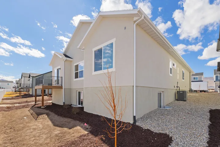 Neutral-toned stucco exterior with multiple windows, an elevated rear deck with black railings, and a gravel and mulch ground cover