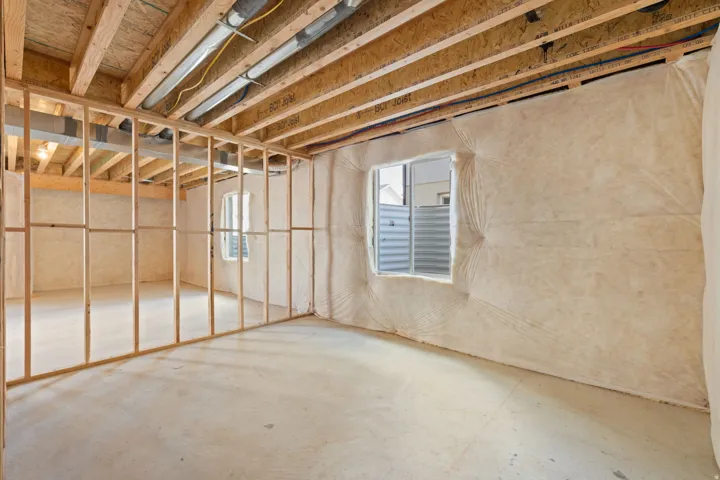 Unfinished lower level featuring wood framing, concrete flooring, and insulated exterior walls with two windows