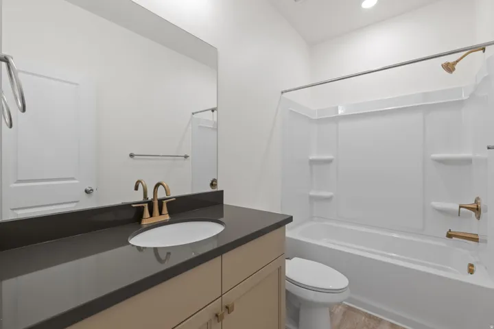 White soaking tub with integrated shelving, brushed brass showerhead and faucet, dark countertop, and light-toned vanity with brass hardware