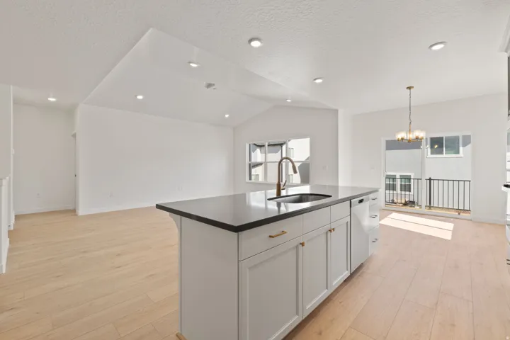Kitchen island featuring a dark countertop, an undermount sink with a bronze-finish faucet, and white cabinetry with gold-tone hardware