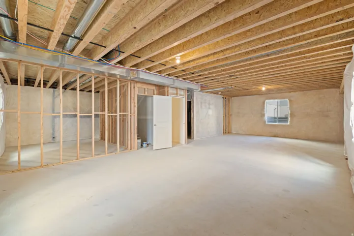 Unfinished lower level featuring concrete flooring, exposed ceiling joists, framed interior walls, and an exterior window
