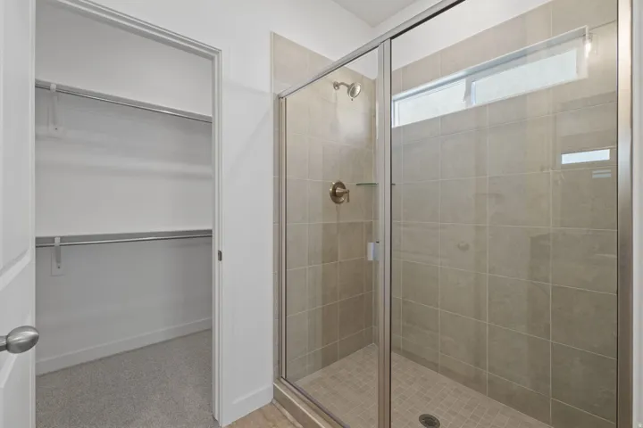 Primary Bathroom featuring a frameless glass-enclosed shower with tile surround, brushed nickel fixtures, and tile flooring