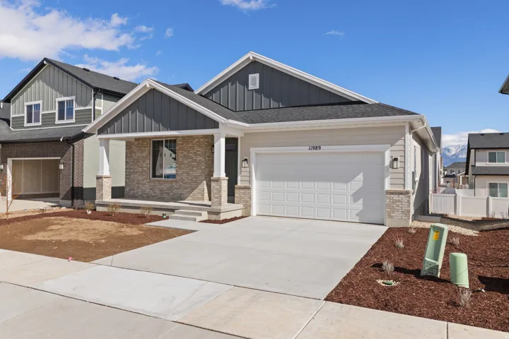 Contemporary exterior featuring light-colored siding, dark gray board and batten accents, a covered porch with stone detailing, a two-car garage, and a concrete driveway