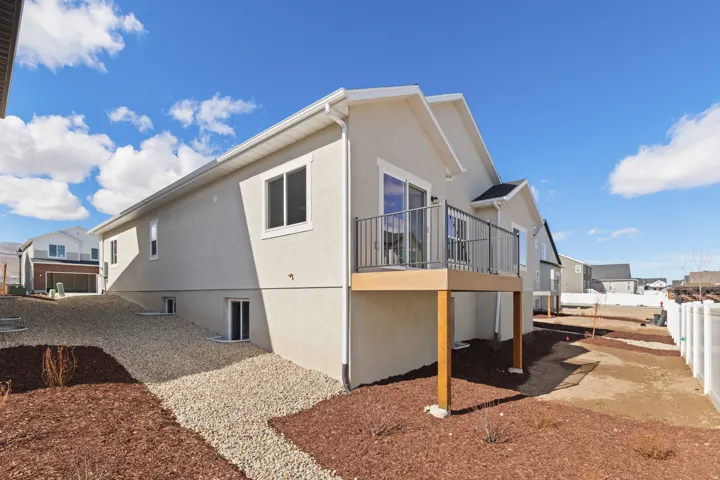 Rear exterior featuring a neutral stucco finish, elevated wood-tone deck with metal railings, and a sliding glass door